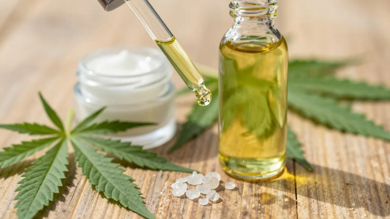 Lahev s CBD olejem, mastí a krystaly na dřevěném povrchu